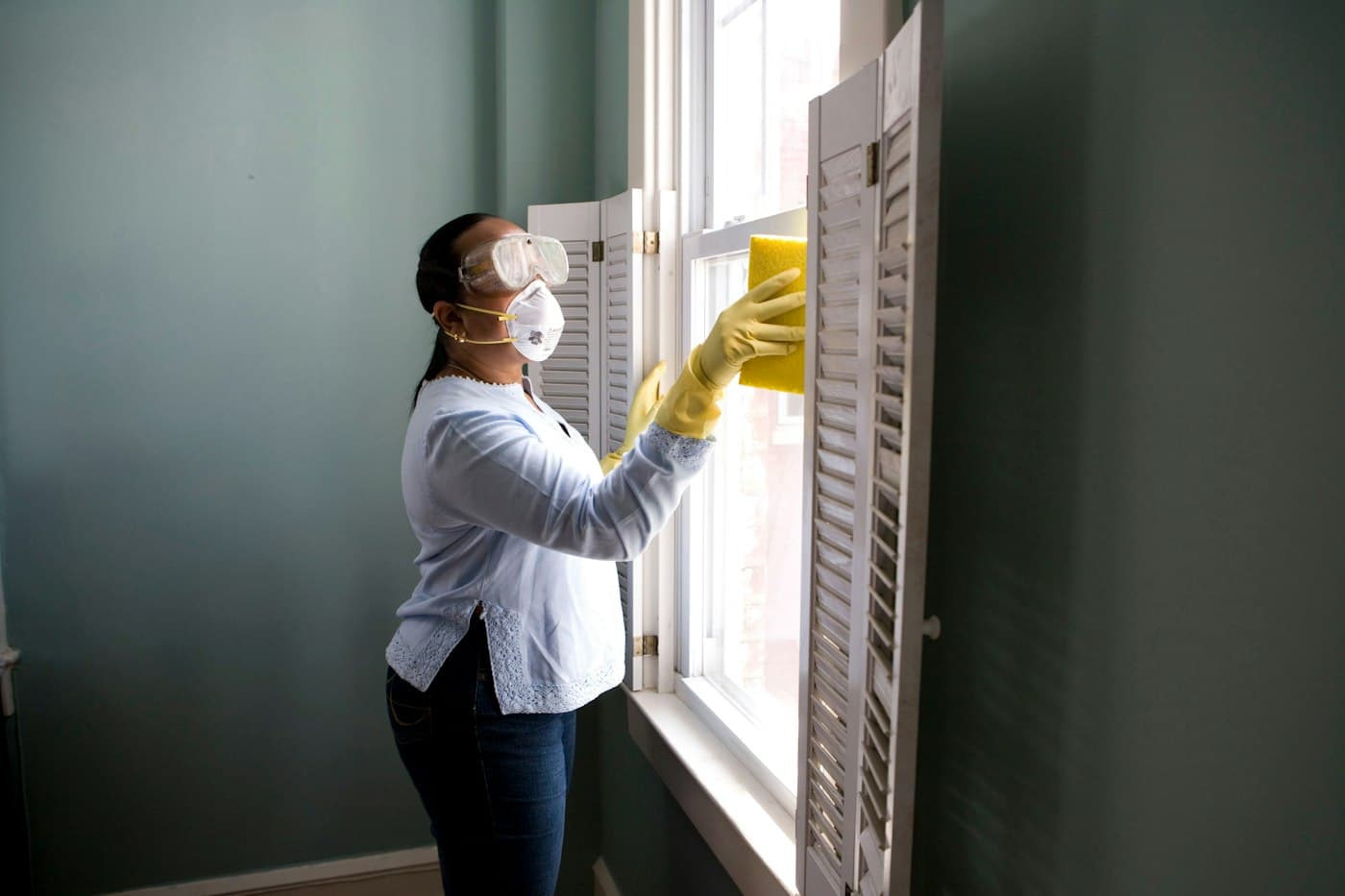 Professional cleaner in gloves wiping a window in a bright home